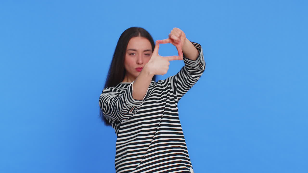 Woman photographer gesturing picture frame with hands looks through fingers focusing cropping image