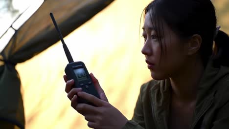 a solitary camper reflects while holding a radio device, encapsulating an introspective moment in nature beneath a tent, surrounded by the tranquility of the wilderness