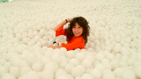 a cute 9-10 years old girl having fun among lots of white ball in a ball pit. 4k slow motion