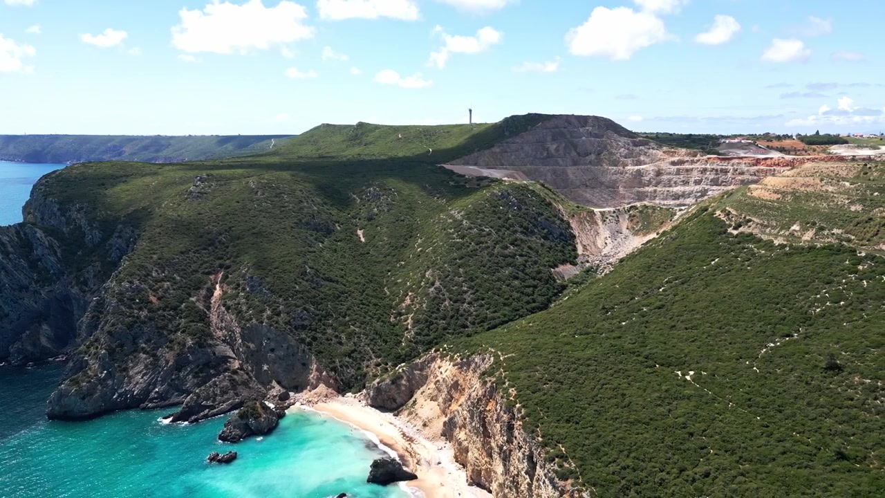 Vista aerea di una spiaggia turchese appartata e scogliere verdi scoscese sotto un cielo azzurro.