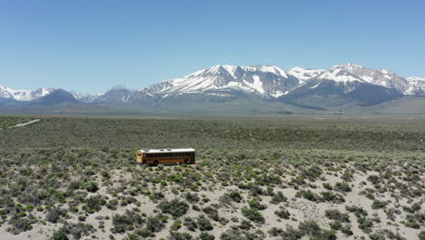 El-Autobús-Escolar-Amarillo-Viaja-A-Través-De-Un-Vasto-Desierto-Con-Montañas-Nevadas-En-La-Distancia.