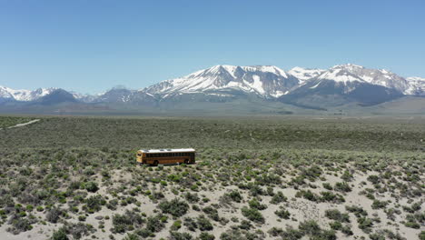 el autobús escolar amarillo viaja a través de un vasto desierto con montañas cubiertas de nieve en la distancia