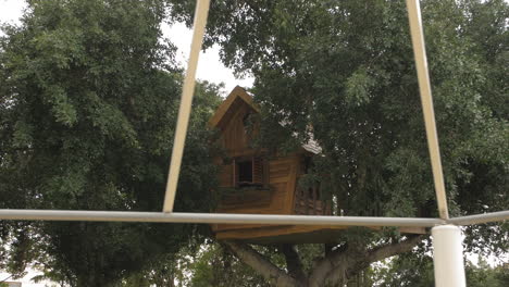 Hermosa-Casa-Del-árbol-Para-Niños,-En-Un-árbol-Grande,-Pasando-Postes-De-Cobertizo,-Carro-En-Cámara-Lenta-A-La-Derecha