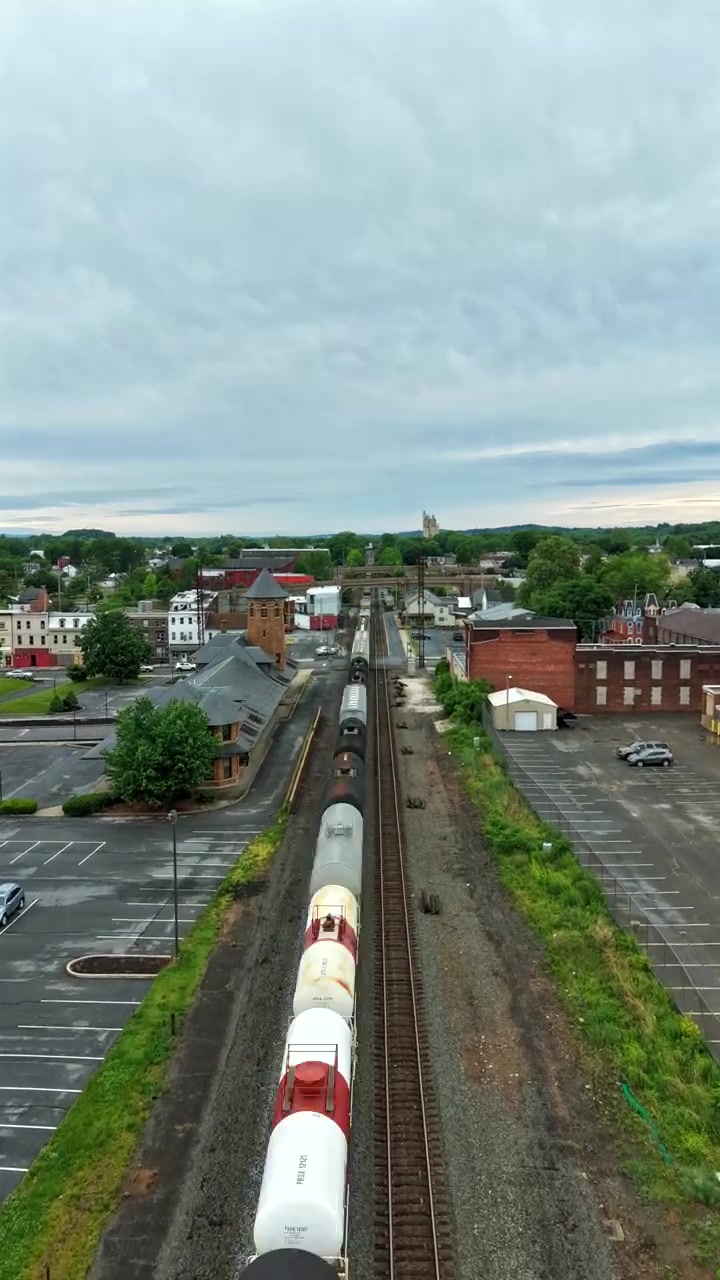 Ripresa aerea con drone dall'alto che mostra container merci e un treno merci in viaggio su un binario ferroviario attraverso un paesaggio suggestivo. Timelapse verticale.