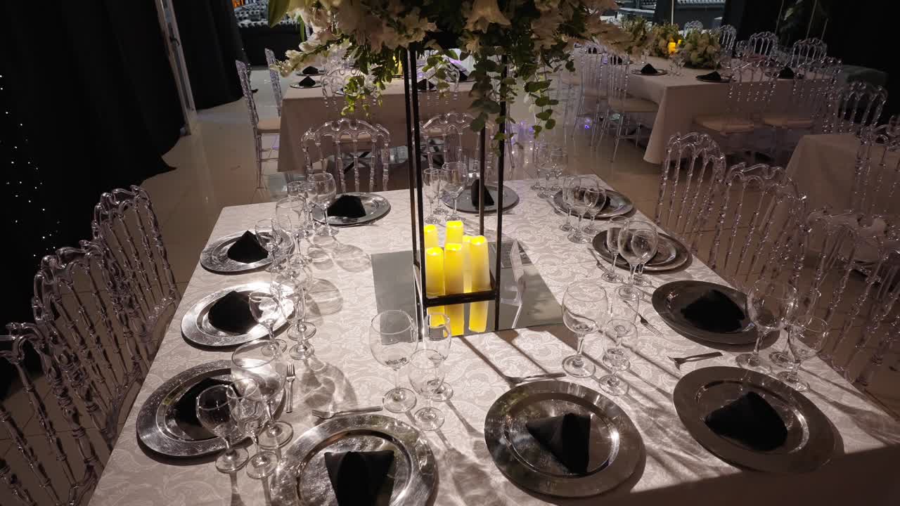Pyntet spisebord med stearinlys, glassfat og arrangert sitteplasser, som skaper en elegant atmosfære for en bryllupsmottakelse i et innendørs lokale.
