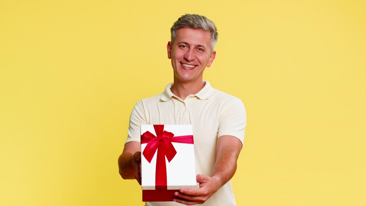 Uomo adulto sorridente che tiene in mano una scatola regalo di compleanno con nastro, offrendo il presente con espressione gentile