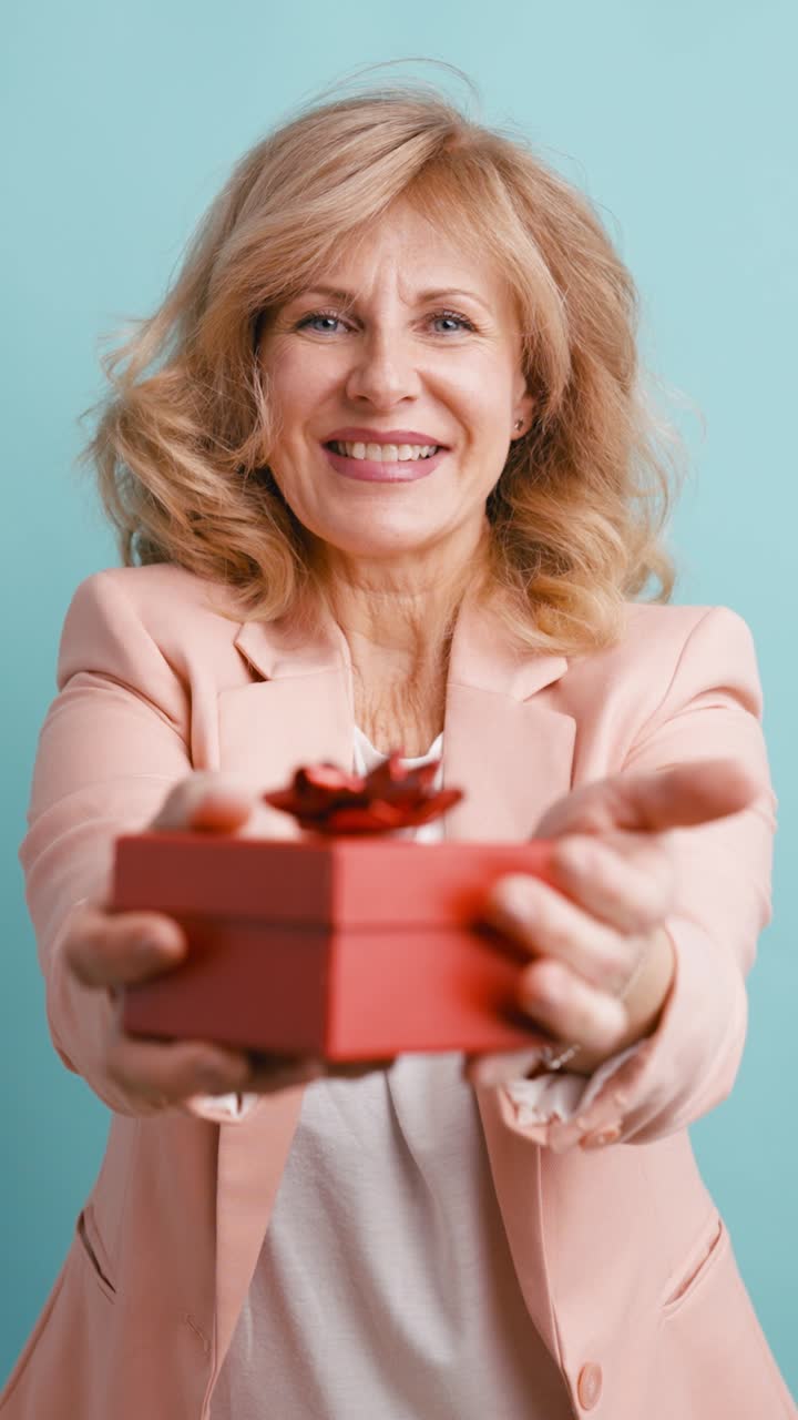 Donna matura felice che offre una scatola regalo rossa