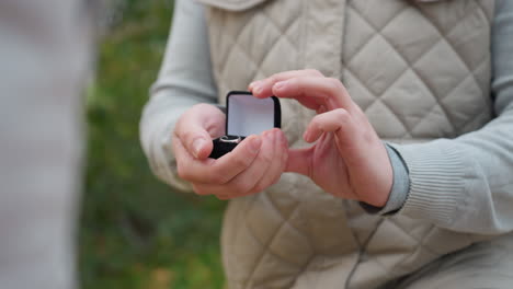 close up of white man on one knee gently holding ring box in both hands preparing for proposal with blurred background of soft greenery and swaying leaves in romantic calm outdoor atmosphere