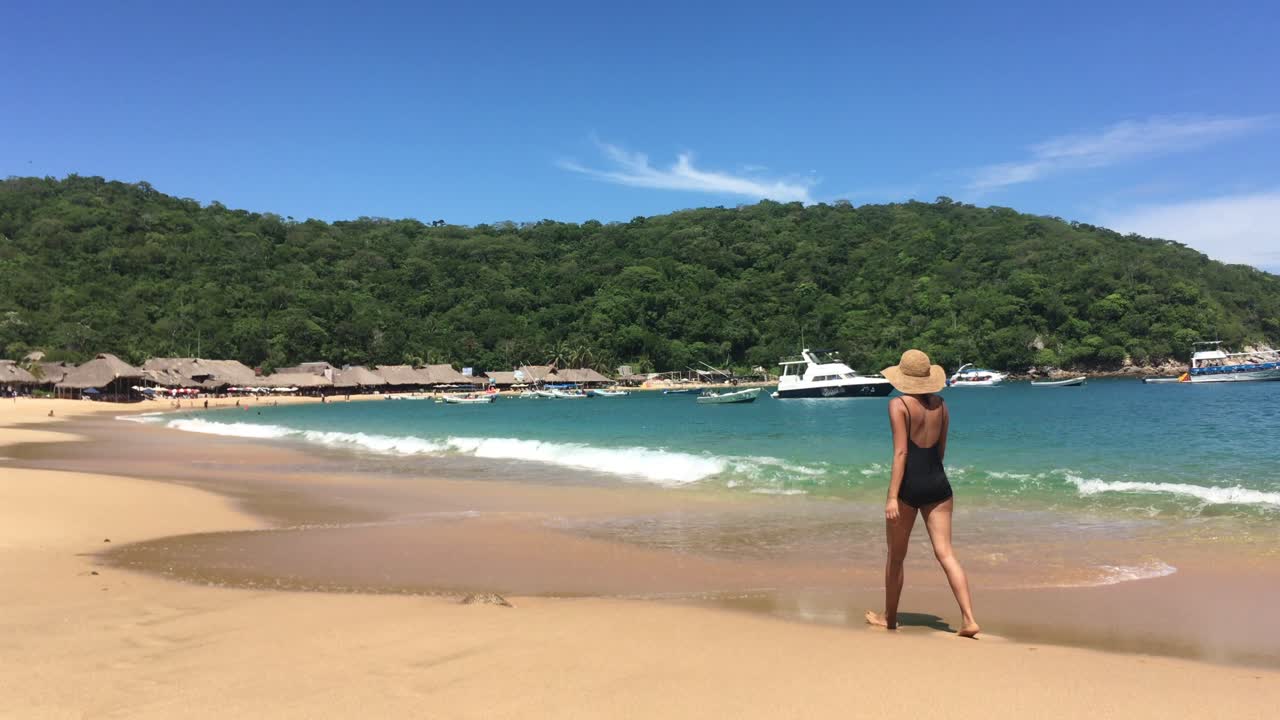 Mulher caminhando na praia, desfrutando do ambiente tropical, do oceano e de barcos na água