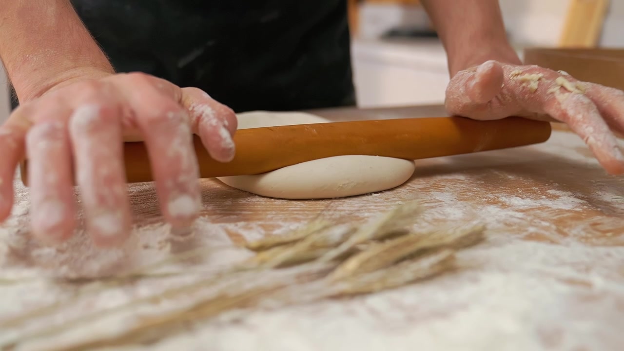 Primo piano di mani che stendono l'impasto con un mattarello di legno su un tavolo infarinato