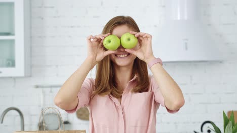 the girl in the white kitchen is having fun with green apples, closing her eyes and smiling