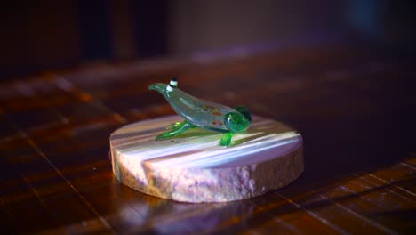 artistic blown-glass frog figurine staged on wooden base with projector light