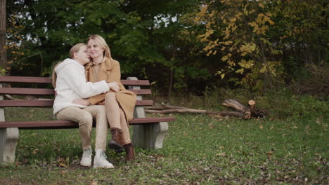 Mom-and-daughter-are-sitting-on-a-bench-in-the-park-on-an-autumn-day