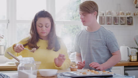 young downs syndrome couple decorating homemade cupcakes with icing in kitchen at home