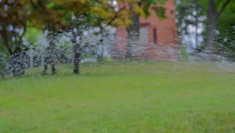 Lawn-water-sprinkler-in-park-watering-the-Türkenschanzpark-in-Vienna-during-a-hot-sunny-day-with-Paulinenwarte-in-the-background