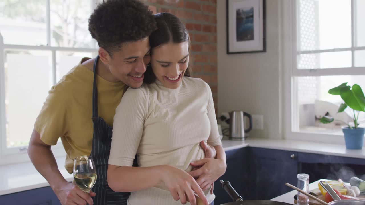 Coppia birazziale felice che cucina insieme e si abbraccia in cucina