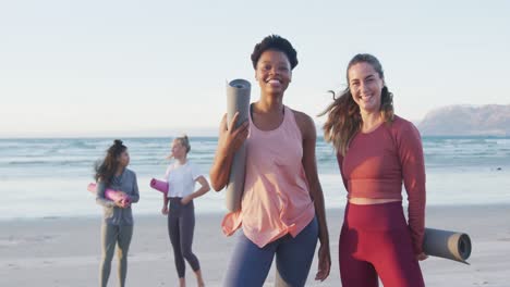 group of diverse female friends holding yoga mats at the beach