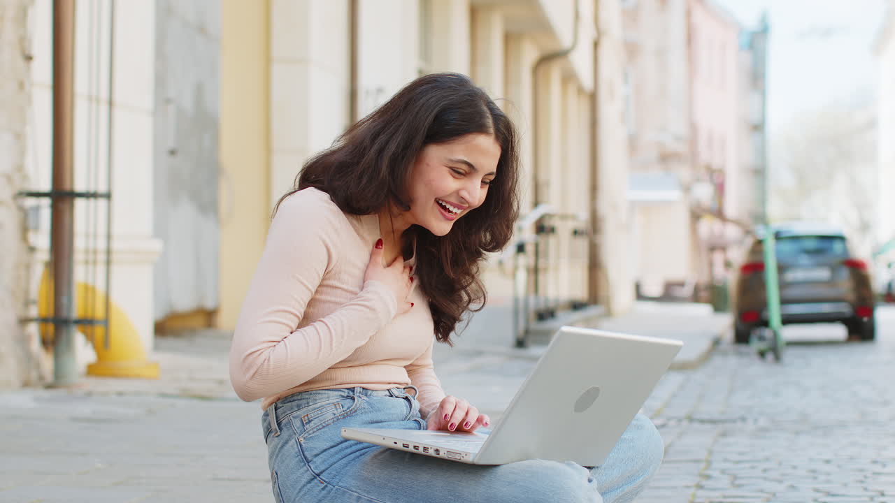 mujer india feliz trabajando en la computadora portátil celebrar el éxito ganar dinero sentado en la calle urbana en la ciudad