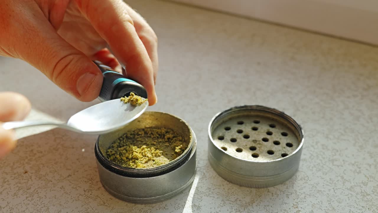 Macro shot of cannabis grinder and man filling ground marijuana into vape tank