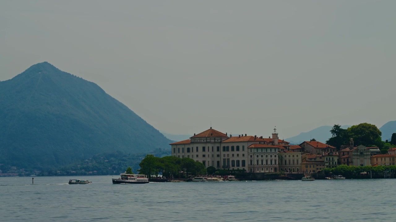 Vista ravvicinata dell'Isola Borromea con affascinanti tetti italiani arancioni, barche che attraversano il Lago Maggiore e una maestosa cima di montagna sullo sfondo