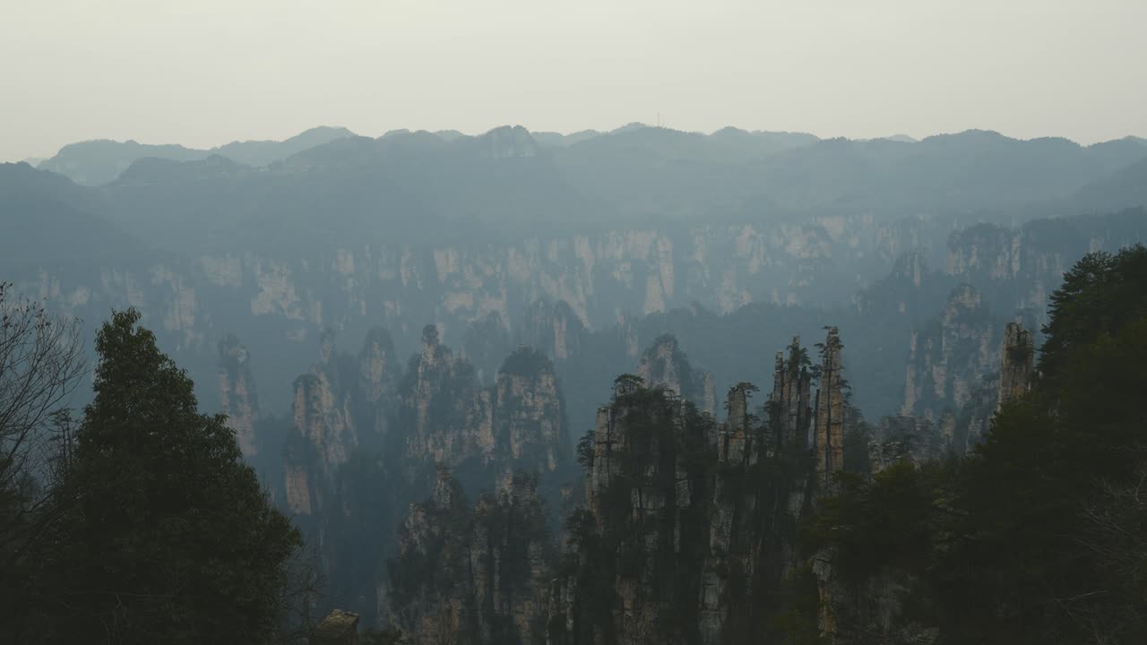 An extensive view over Zhangjiajie’s renowned rock pillars, set against layers of misty mountains fading into the evening light, highlighting the surreal beauty of this Chinese landmark