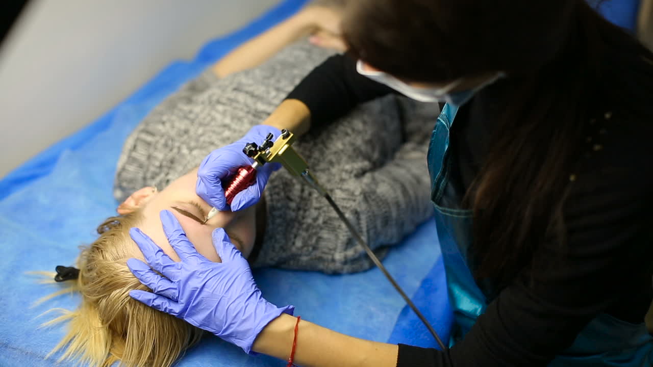 Beautician hands doing eyebrow tattoo on woman face