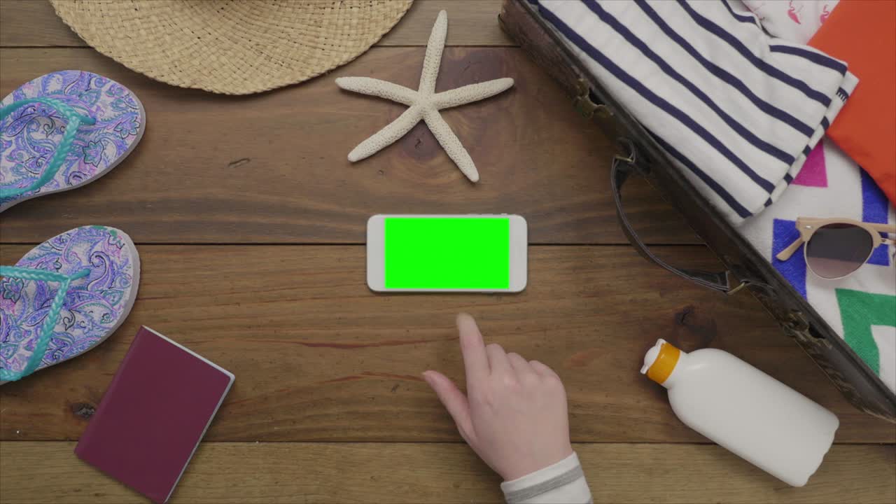 imágenes aéreas de una mujer tocando un teléfono inteligente junto a los suministros de la playa.