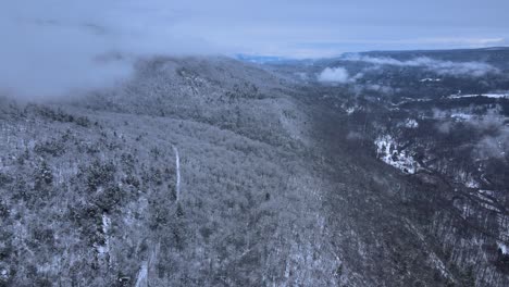 flying through clouds over snow-covered mountains and forests in a beautiful mountain valley during winter on a cloudy day