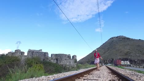 mujer caminando por las vías del tren cerca de las ruinas del antiguo castillo