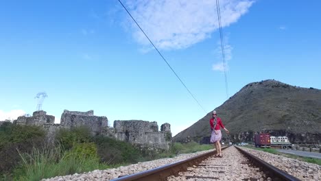 woman walking on train tracks near ancient castle ruins