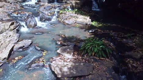 Aerial-shot-of-a-sunny-small-rocky-river,-water-flowing