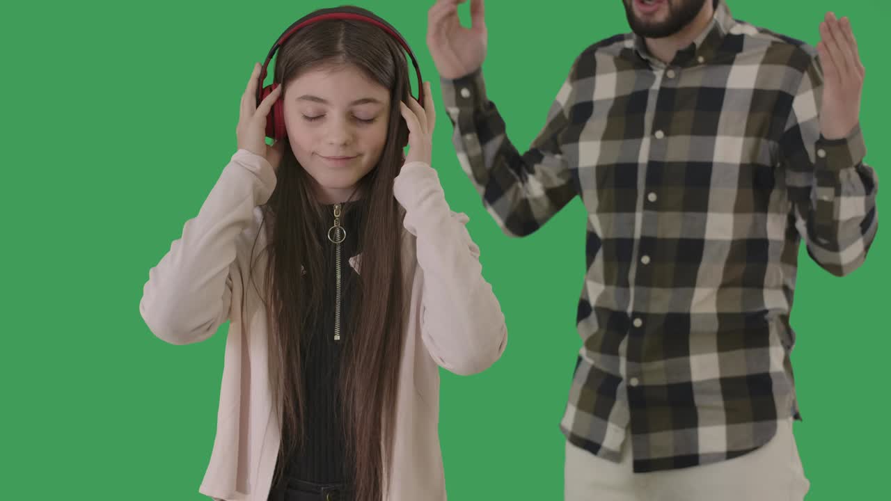 retrato de una adolescente caucásica despreocupada escuchando música en auriculares como un hombre irreconocible gestando en el fondo. hija ignorando al padre regañándola. chromakey. cine 4k prores hq.
