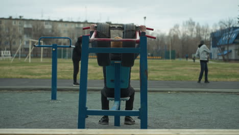 close-up of a coach gripping workout equipment while exercising outdoors,two boys are also working out on a track near a grassy field, with people visible in the background