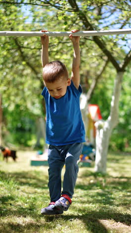cheerful caucasian baby boy hanging on the horizontal bar swinging. toddler doing sport outdoors. vertical video.