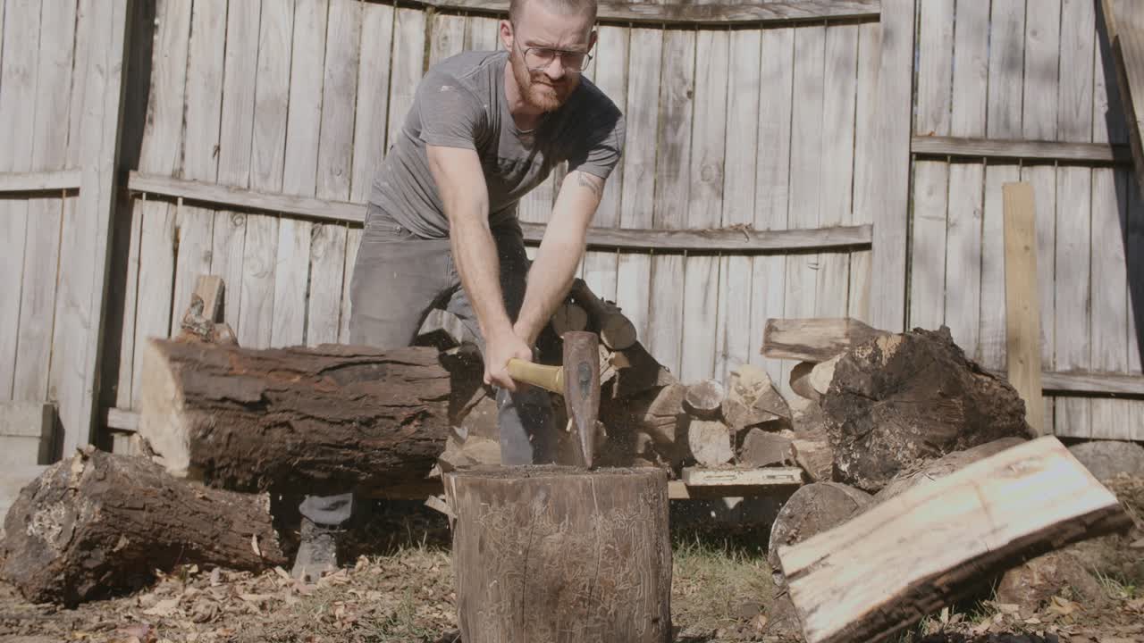 Slow motion-optagelse af en mand i sin baghave, der kløver et brændestykke