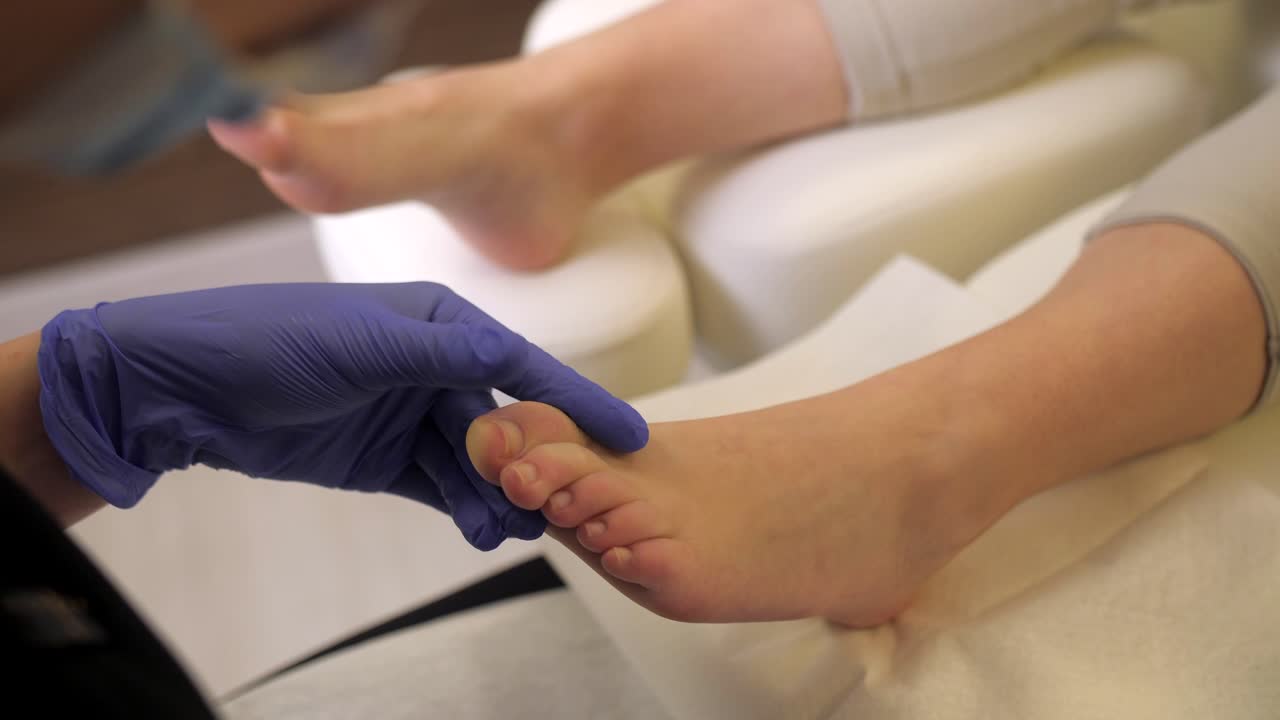 un pedicurista profesional limpia la cutícula de las uñas de los dedos del pie femenino con guantes y herramientas