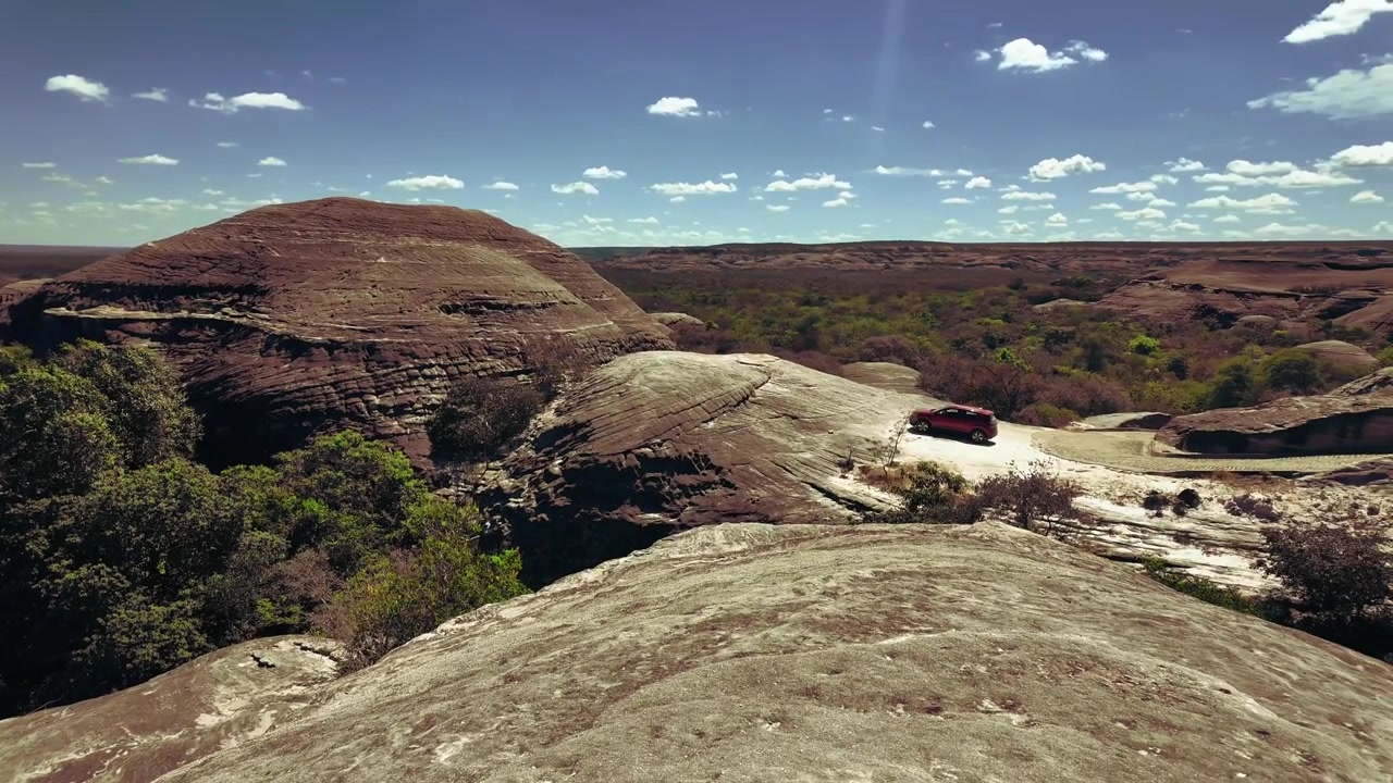 Striated sandstone cliff face shows natural stone bedding lines with sparse green shrubs at Serra das Confusoes National Park under a bright sky