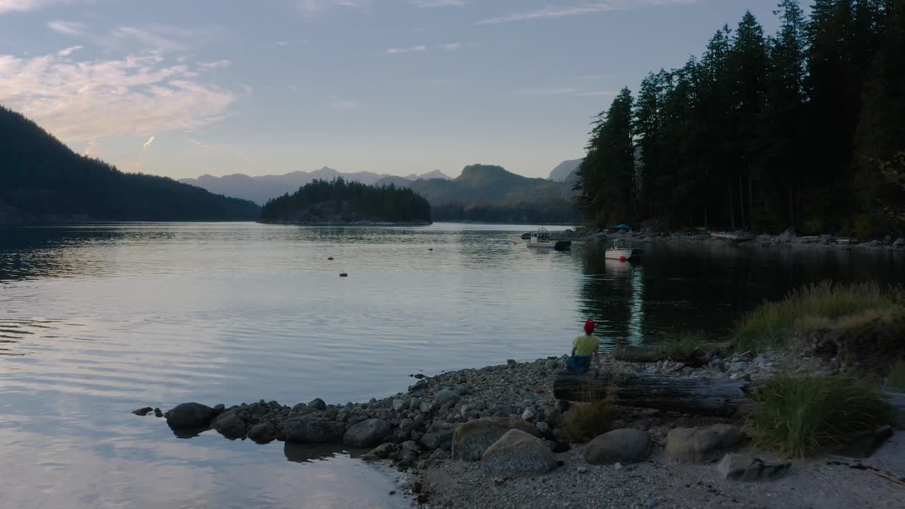 женщина сидит на бревне дерева и наслаждается видом на залив сехелт во время заката на побережье саншайн возле эгмонта, британская колумбия, канада