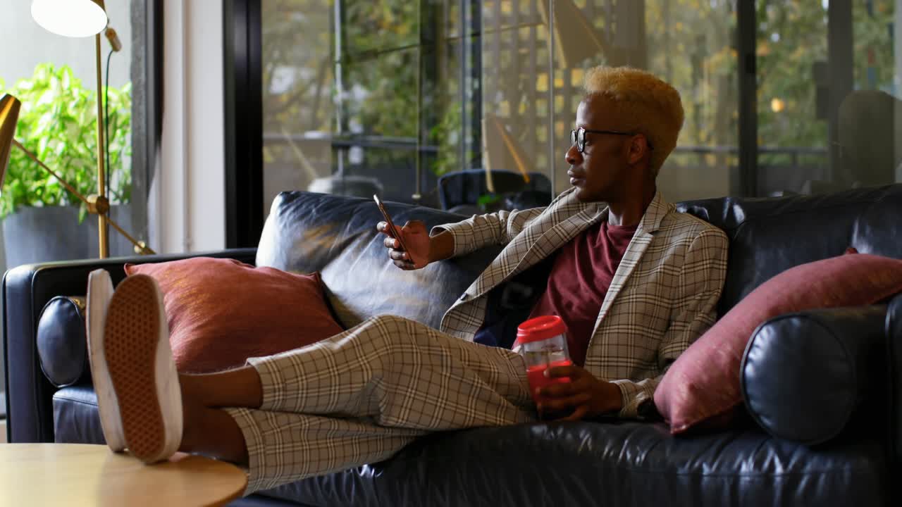 Giovane uomo d'affari afroamericano che guarda il cellulare in un ufficio moderno 4k