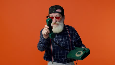 Senior-bearded-gray-haired-man-talking-on-wired-vintage-telephone-of-80s,-says-hey-you-call-me-back