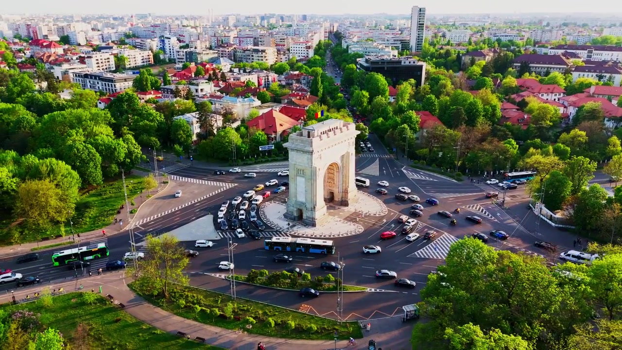 Órbita de drone ao redor do Arcul de Triumf revelando um extenso parque verde e a paisagem urbana circundante