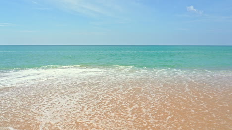 Panning-right-on-Beautiful-clean-white-foamy-sea-waves-crashing-against-an-empty-yellow-sand-beach-at-daytime