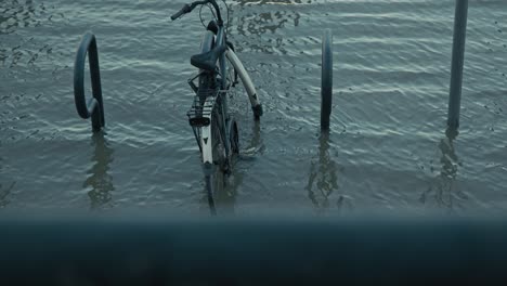 submerged bike in flooded waters near a bike rack along the riverbank