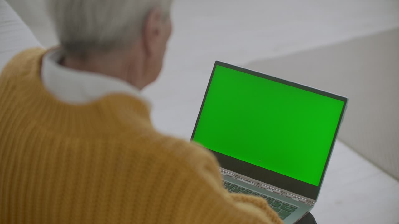 una mujer mayor mira un monitor con una pantalla verde y habla a través de un enlace de video con su nieta o hija o un médico. ayuda de video para los ancianos. la abuela usa una computadora portátil