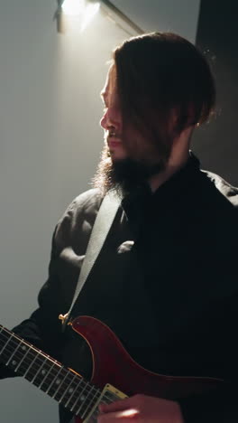 guitarist in black attire passionately plays red electric guitar against stark white backdrop, camera zooming out