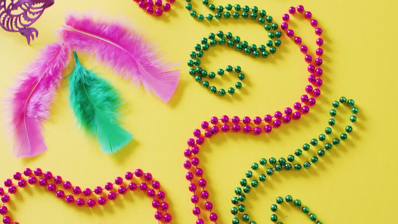 video de máscara rosa, cuentas de carnaval de mardi gras y plumas sobre fondo amarillo con espacio para copiar