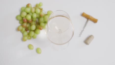 vaso de vino blanco, sacacorchos y uvas sobre una superficie blanca con espacio para copiar