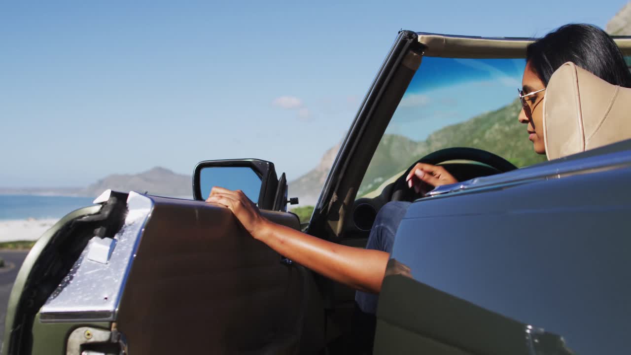 mujer afroamericana con gafas de sol saliendo de un coche descapotable en la carretera