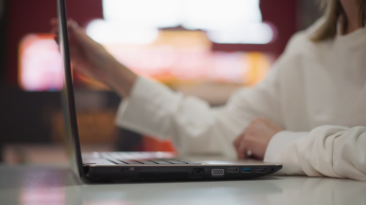 primer plano de una computadora portátil cerrada por una persona en un entorno de centro comercial moderno, el fondo vibrante borroso crea un ambiente urbano, dinámico y profesional