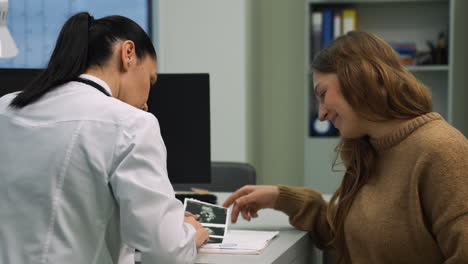mujer mostrando un sonograma al médico